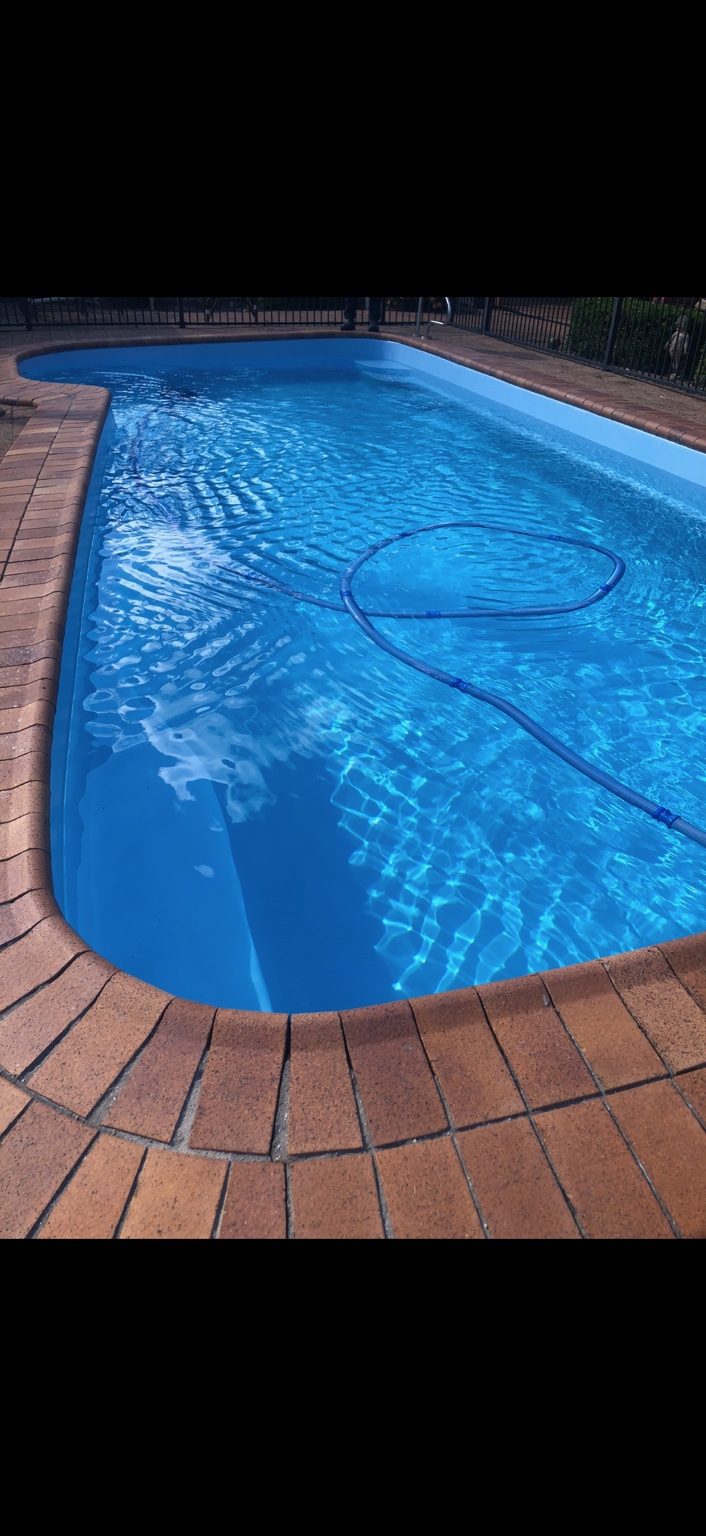 Filled blue swimming pool with curved brick edging